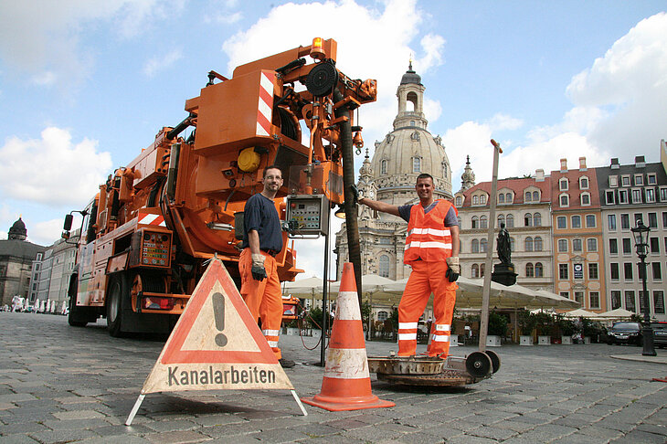 Dieses Bild zeigt einen Mitarbeiter der Stadtentwässerung bei Kanalarbeiten. Im Hintergrund befindet sich ein Fahrzeug der Stadtentwässerung und die Dresdner Frauenkirche.