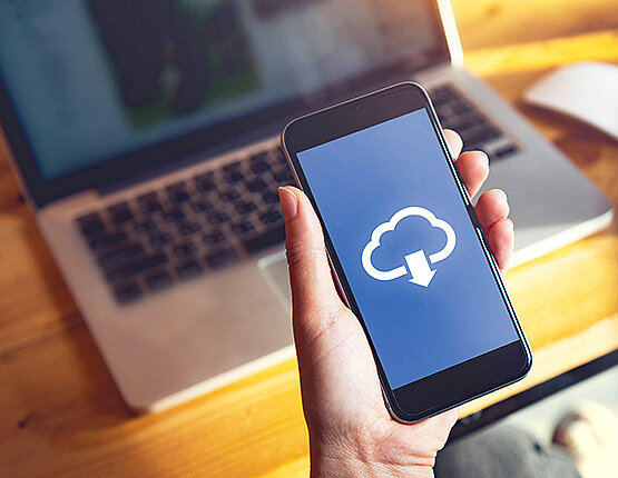 Dieses Bild zeigt eine Hand die ein Smartphone in der Hand hält. Auf dem Display ist das Downloadsymbol zu sehen.