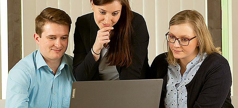 Das Bild zeigt drei Beschäftigte der Stadtentwässerung Dresden GmbH, die auf einen Laptop schauen.