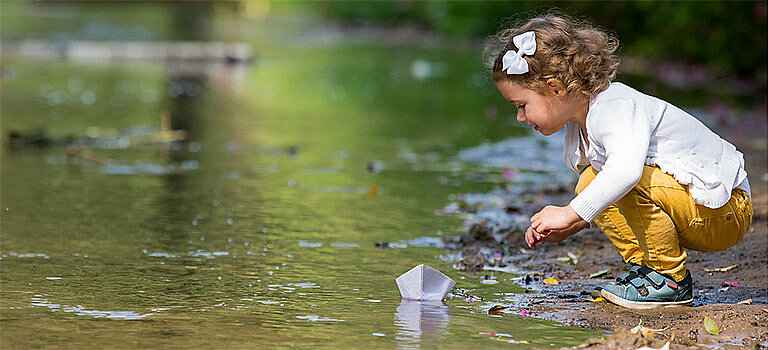 Auf dem Bild spielt ein kleines Mädchen an einem sauberen Bach.